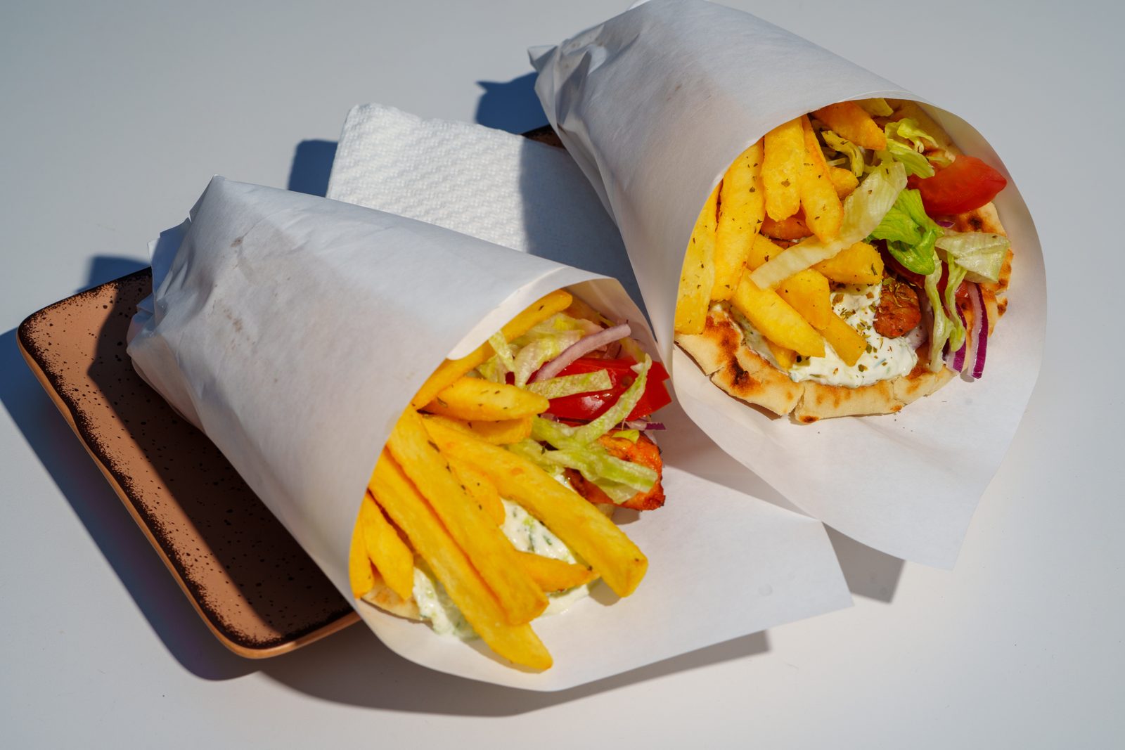 Two authentic Greek pita gyros with fries inside, wrapped in white paper at Kreta Greek Gyros and Grill, Paceville Malta
